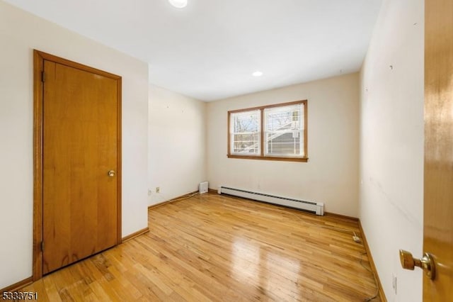 empty room featuring a baseboard heating unit and light hardwood / wood-style flooring