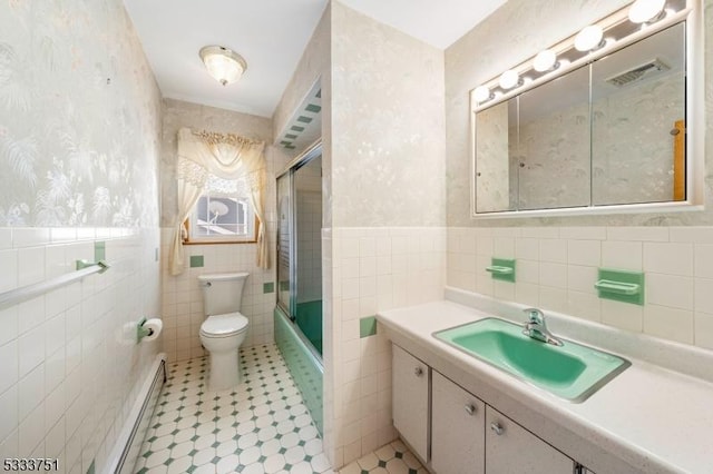 full bathroom featuring tile walls, shower / bath combination with glass door, vanity, baseboard heating, and toilet