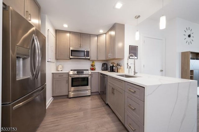 kitchen featuring stainless steel appliances, sink, hanging light fixtures, kitchen peninsula, and hardwood / wood-style flooring