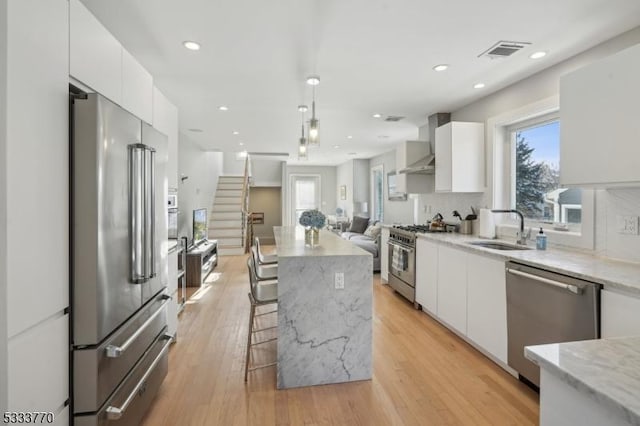 kitchen with white cabinetry, high end appliances, sink, pendant lighting, and wall chimney exhaust hood