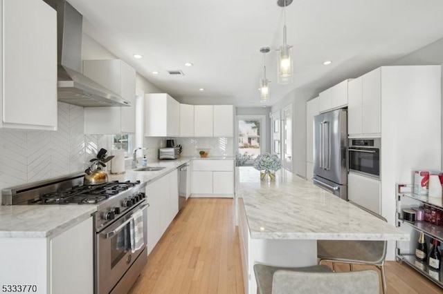 kitchen with pendant lighting, sink, white cabinets, wall chimney range hood, and stainless steel appliances