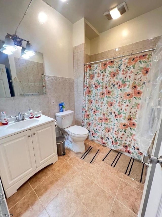 bathroom featuring toilet, vanity, tile patterned floors, and tile walls