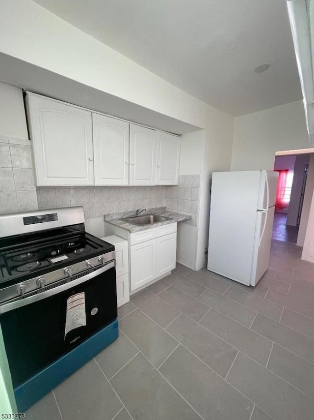 kitchen with white cabinetry, tile patterned floors, stainless steel range with gas stovetop, backsplash, and white refrigerator