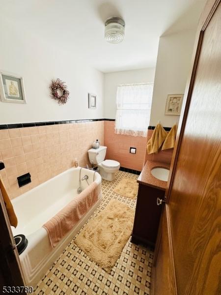 bathroom featuring tile walls, a bathtub, tile patterned flooring, vanity, and toilet