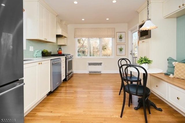 kitchen with tasteful backsplash, hanging light fixtures, radiator, stainless steel appliances, and white cabinets