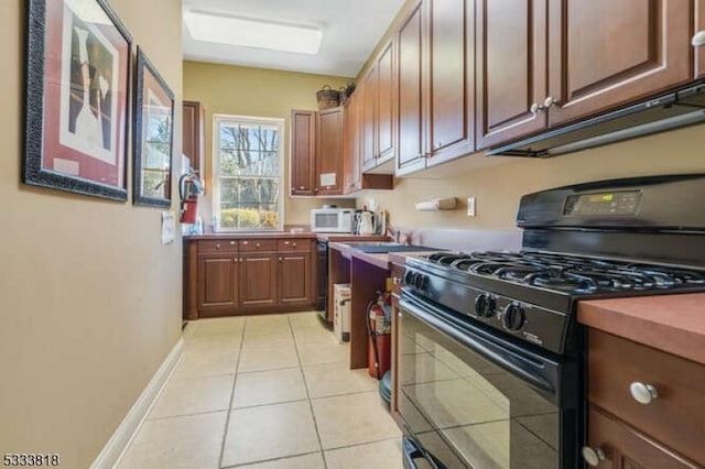 kitchen with black gas range oven, white microwave, light tile patterned floors, and baseboards