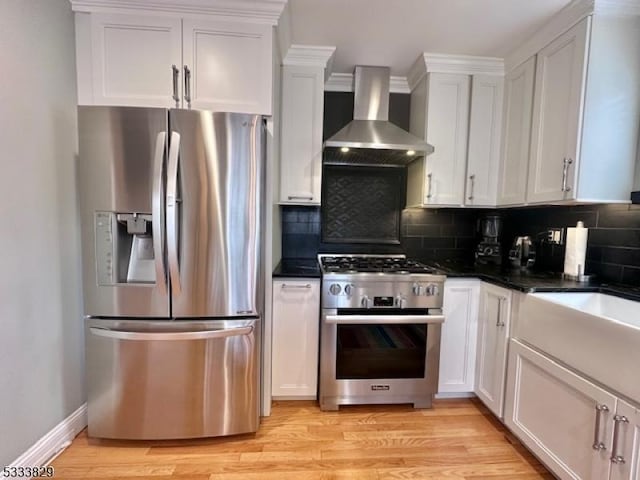 kitchen with wall chimney range hood, white cabinets, stainless steel appliances, and light wood-type flooring