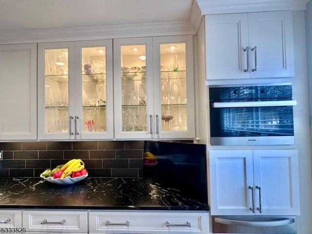 bar featuring white cabinetry, decorative backsplash, dark stone countertops, and oven