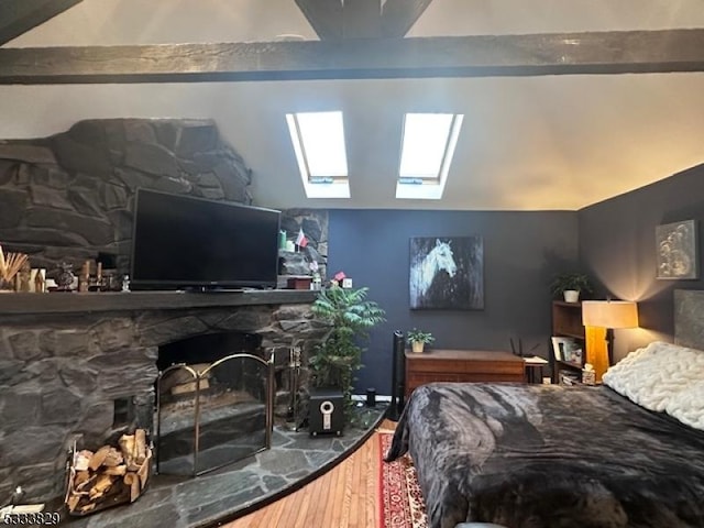 bedroom with vaulted ceiling with skylight, hardwood / wood-style floors, and a stone fireplace