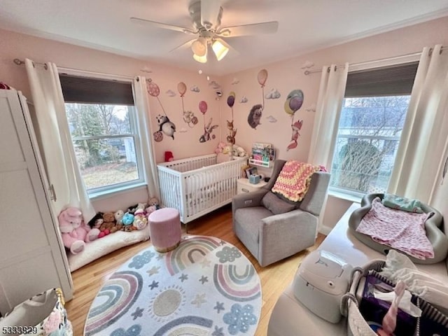 bedroom featuring ceiling fan, light wood-type flooring, radiator heating unit, and a crib