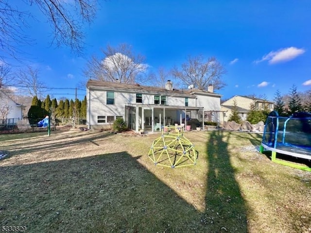 rear view of property with a trampoline and a yard