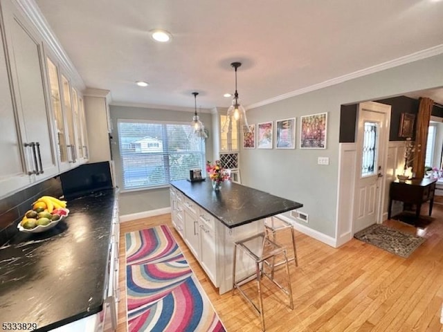 kitchen featuring a breakfast bar area, light wood-type flooring, hanging light fixtures, ornamental molding, and white cabinets