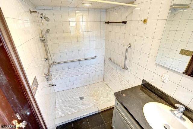 bathroom with tile patterned flooring, vanity, a tile shower, and tile walls