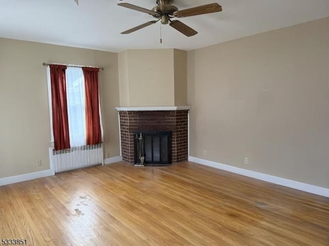 unfurnished living room with radiator, a fireplace, ceiling fan, and light wood-type flooring