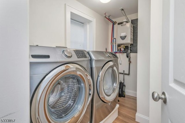 clothes washing area featuring washer and clothes dryer, water heater, and light wood-type flooring