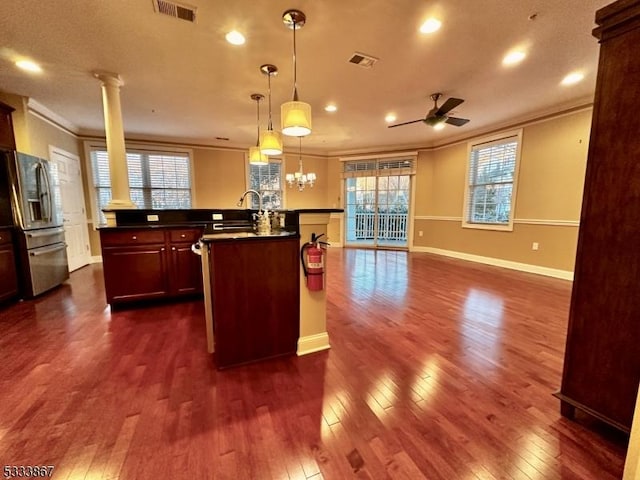 kitchen featuring sink, stainless steel fridge, ornamental molding, an island with sink, and decorative light fixtures