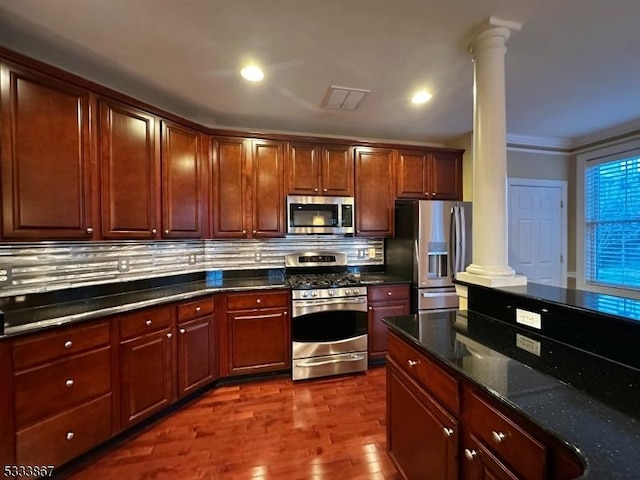 kitchen featuring dark wood-type flooring, appliances with stainless steel finishes, tasteful backsplash, dark stone counters, and ornate columns