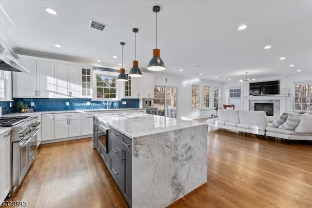 kitchen with hanging light fixtures, white cabinetry, light stone counters, a kitchen island, and stainless steel appliances