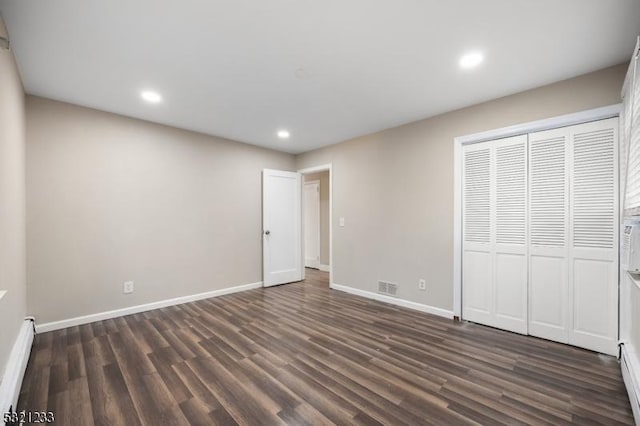 unfurnished bedroom with baseboard heating, dark hardwood / wood-style floors, and a closet