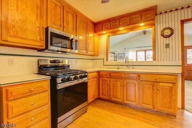 kitchen featuring kitchen peninsula, light hardwood / wood-style flooring, appliances with stainless steel finishes, sink, and lofted ceiling