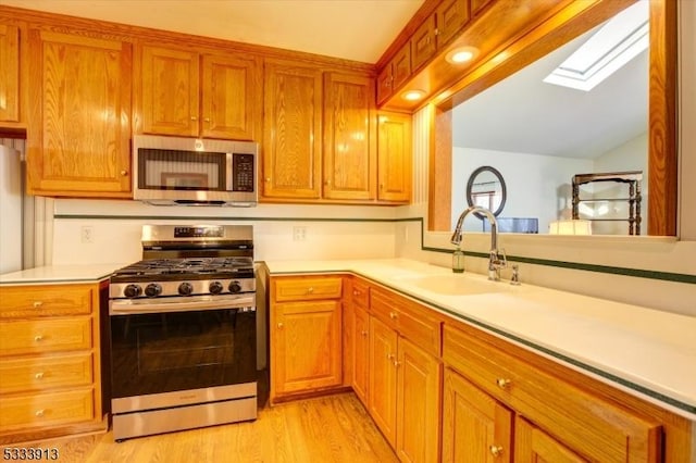 kitchen with sink, light wood-type flooring, vaulted ceiling with skylight, and appliances with stainless steel finishes