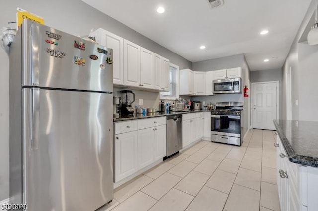 kitchen with light tile patterned floors, appliances with stainless steel finishes, dark stone counters, and white cabinets