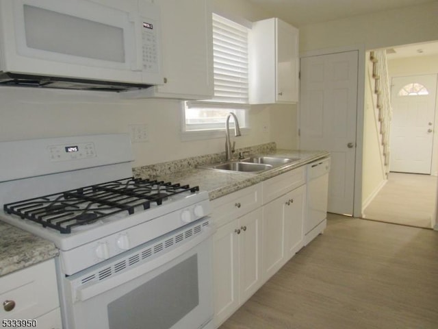 kitchen featuring white appliances, a sink, white cabinets, light wood-style flooring, and light stone countertops