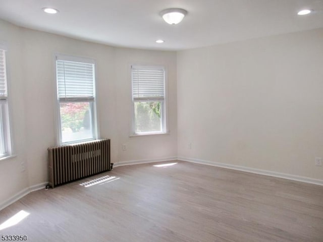 unfurnished room featuring radiator, light wood-type flooring, baseboards, and recessed lighting