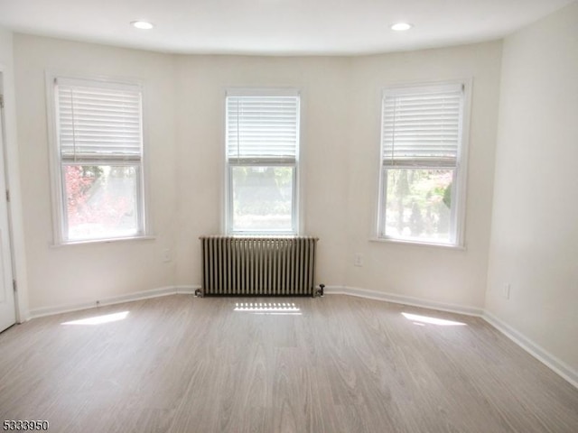 unfurnished room with radiator heating unit, wood finished floors, healthy amount of natural light, baseboards, and recessed lighting