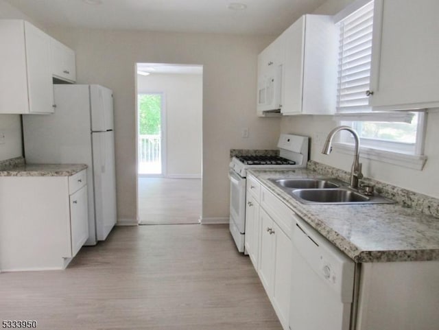 kitchen with white appliances, a sink, light wood finished floors, baseboards, and white cabinetry