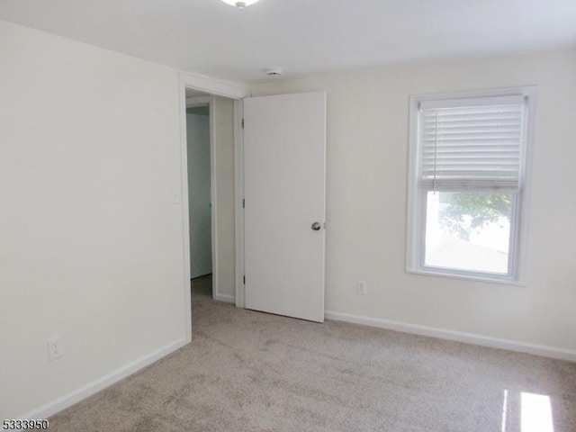 spare room featuring light carpet and baseboards