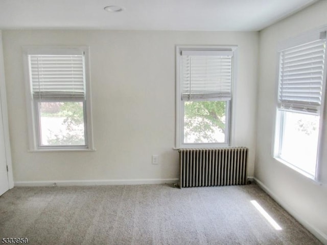 carpeted empty room with radiator, plenty of natural light, and baseboards