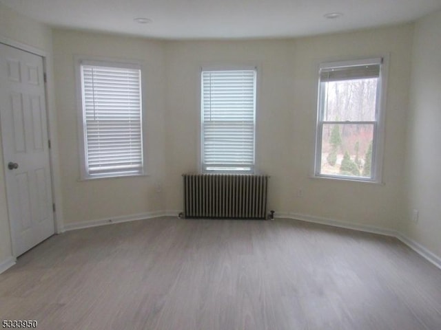 spare room with radiator heating unit, light wood finished floors, and baseboards