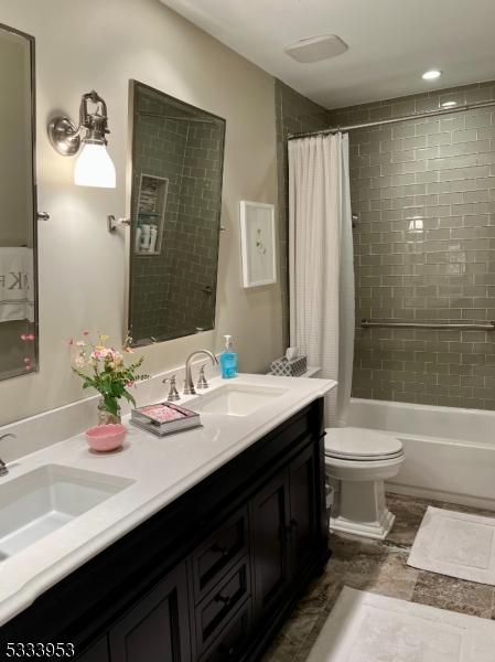 bathroom with double vanity, toilet, shower / bath combo with shower curtain, and a sink