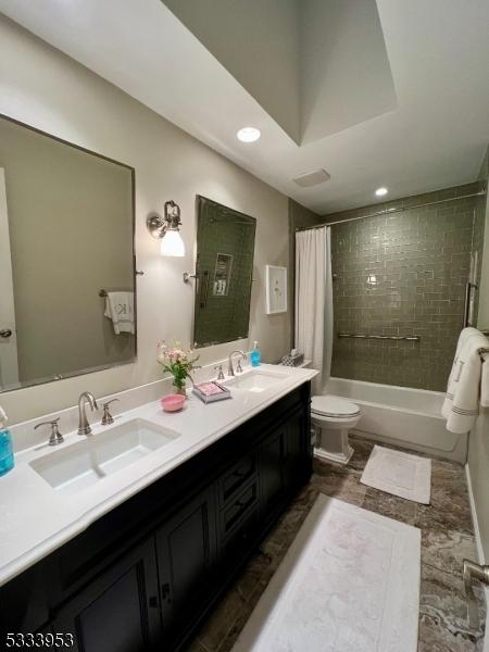 bathroom featuring double vanity, shower / tub combo, toilet, and a sink