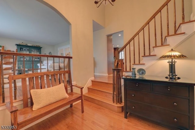 sitting room with baseboards, a high ceiling, arched walkways, stairs, and light wood-style floors