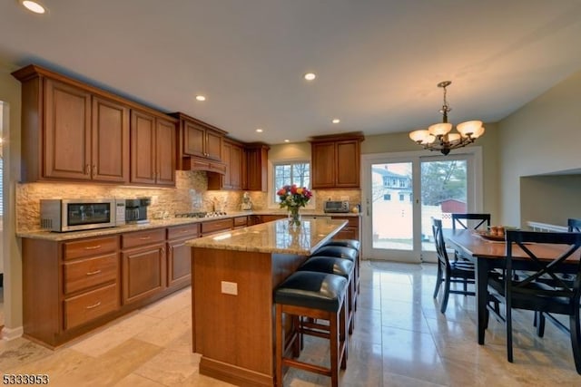 kitchen featuring backsplash, a center island, appliances with stainless steel finishes, an inviting chandelier, and light stone countertops