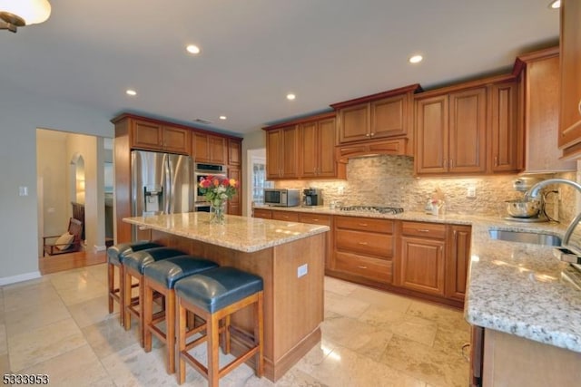 kitchen featuring light stone counters, a kitchen island, stainless steel appliances, a sink, and backsplash