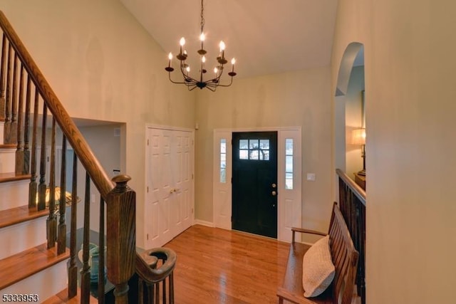 foyer featuring stairway, wood finished floors, arched walkways, a notable chandelier, and high vaulted ceiling