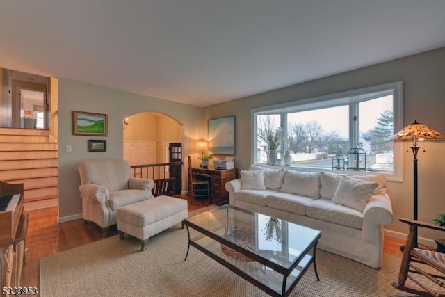 living area with arched walkways, baseboards, and wood finished floors