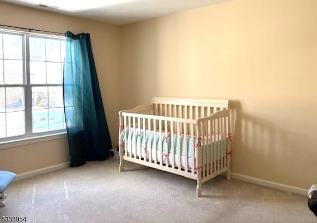 unfurnished bedroom with a nursery area, carpet flooring, visible vents, and baseboards