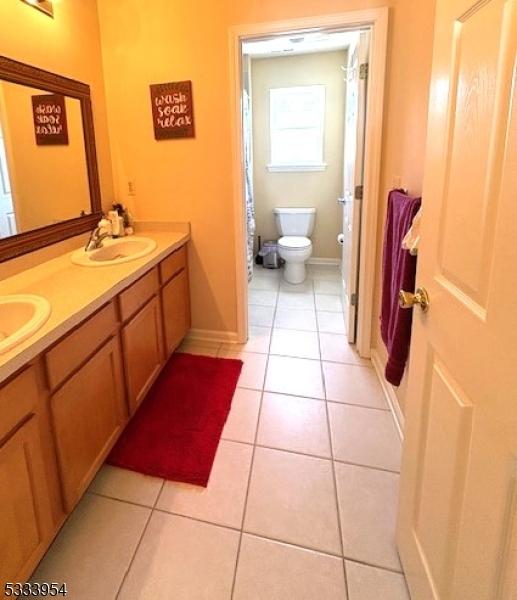 bathroom with toilet, tile patterned flooring, double vanity, and a sink