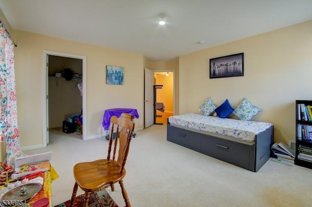 bedroom with a closet, light carpet, a spacious closet, and baseboards