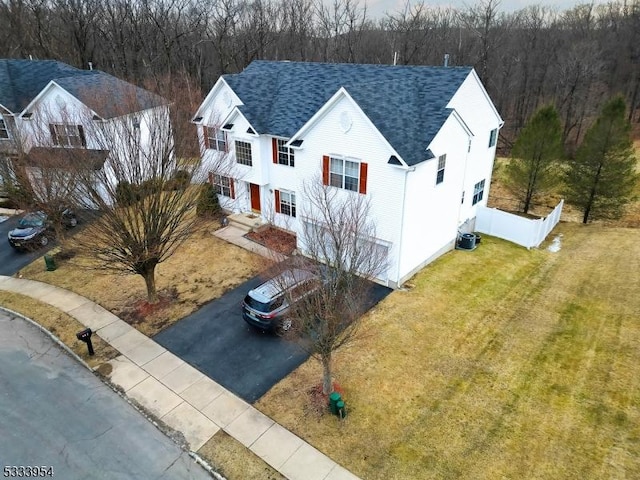 view of front facade featuring driveway, a shingled roof, fence, cooling unit, and a front lawn