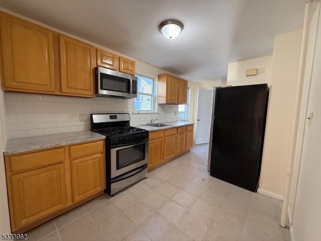 kitchen featuring light stone countertops, appliances with stainless steel finishes, sink, and backsplash