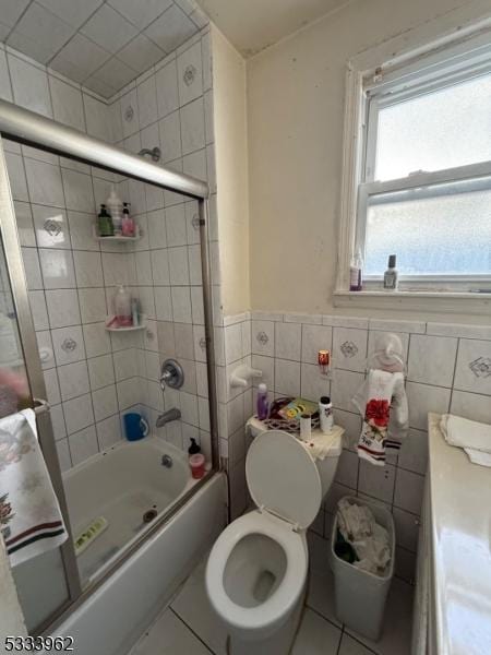 full bathroom featuring combined bath / shower with glass door, tile patterned flooring, tile walls, vanity, and toilet