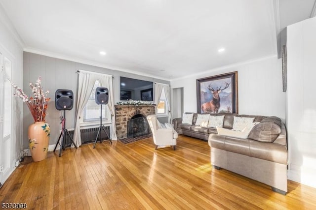 living room with wood-type flooring, a stone fireplace, radiator, and crown molding