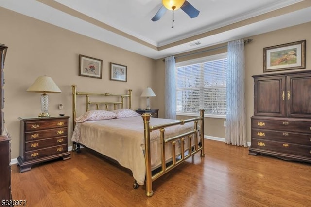 bedroom with ornamental molding, a tray ceiling, ceiling fan, and light hardwood / wood-style flooring