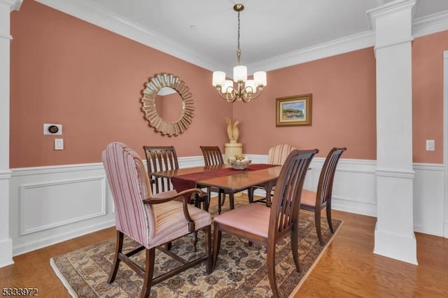 dining space featuring ornate columns, crown molding, hardwood / wood-style floors, and an inviting chandelier