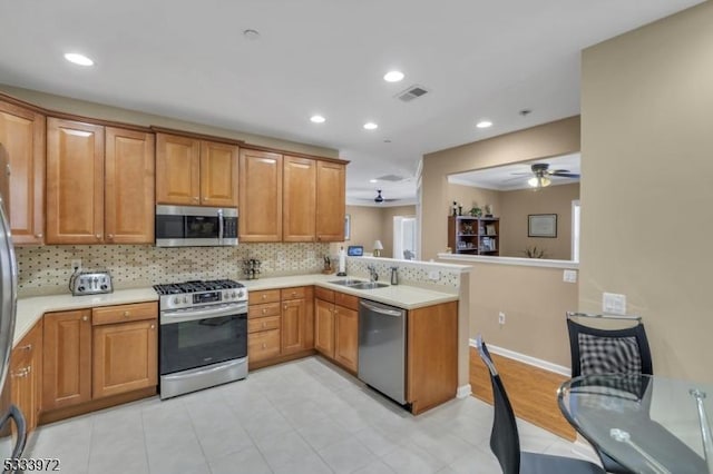 kitchen with sink, ceiling fan, backsplash, stainless steel appliances, and kitchen peninsula